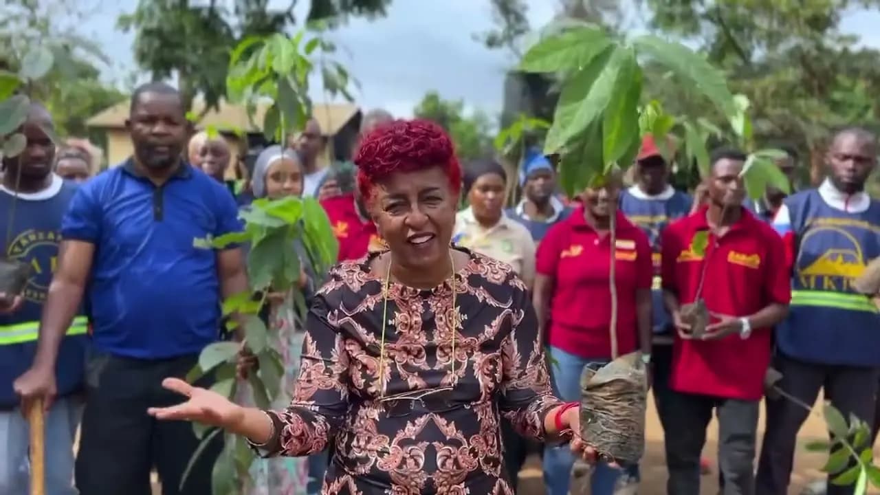 Zainab Ansell holding a tree seedling and speaking to a crowd of staff and community members at a planting day.