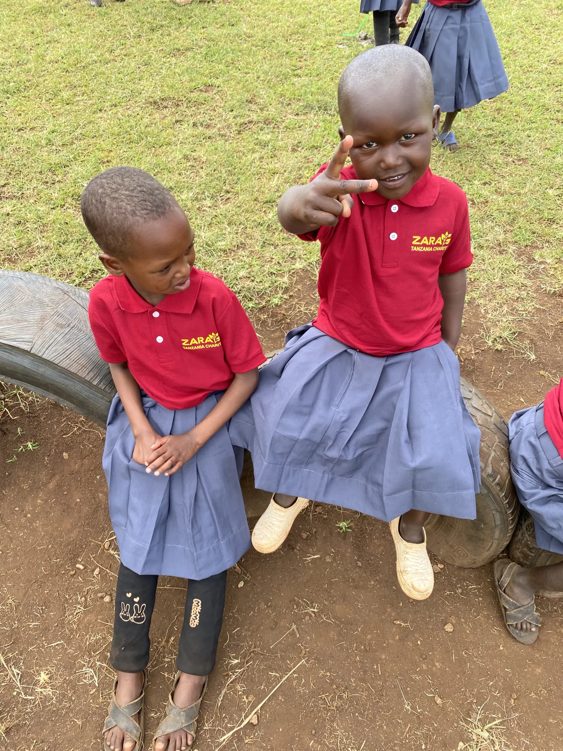 Two children sitting on a tractor tyre in the school yard, one pointing at the camera and laughing.