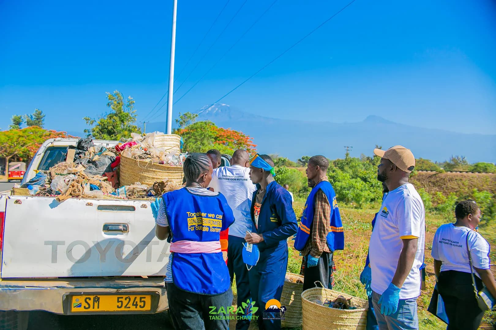 A pickup truck piled high with sacks of collected waste at the end of a cleanup day, Mount Kilimanjaro on the horizon behind the volunteers.